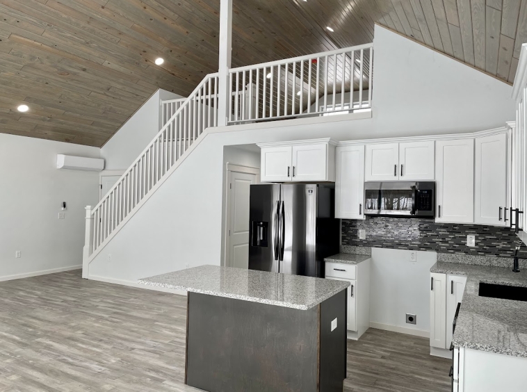 White kitchen in open concept modular chalet with finished attic loft space, white railings, and LVP flooring