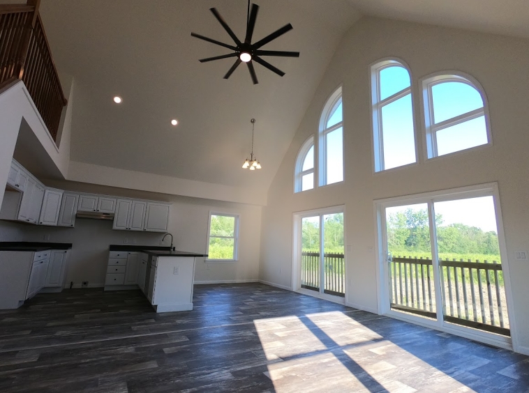 Vaulted ceiling in modular chalet with open concept floor plan and balcony overlooking the white U-shaped kitchen.